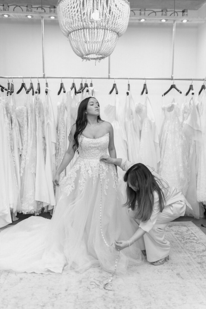 Bride trying on wedding dress during fitting at Candè Bridal Boutique Kelowna with seamstress adjusting gown